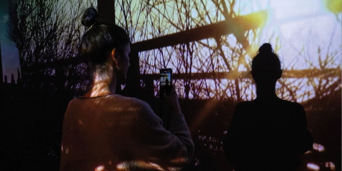 Eine Frau fotografiert ihren eigenen Schatten während eine multimedialen Kunstausstellung.